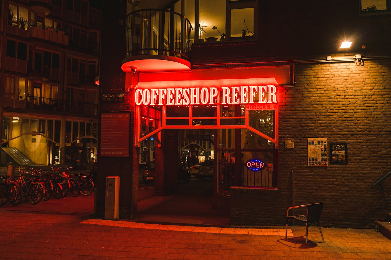 Nighttime view of Coffeeshop Reefer's vibrant neon entrance in Amsterdam, Netherlands.