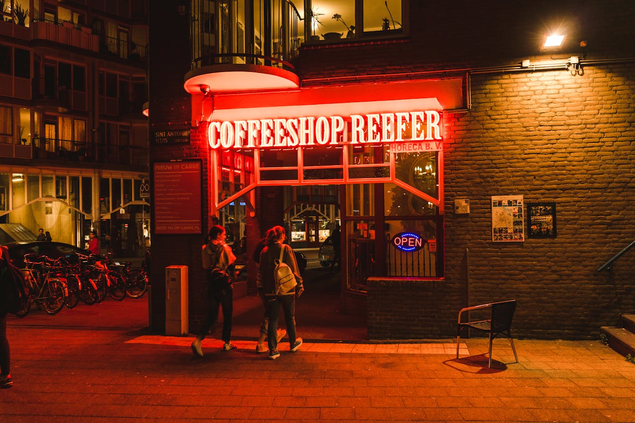 Neon-lit entrance of Coffeeshop Reefer in Amsterdam, capturing night city life.